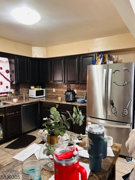 kitchen featuring tasteful backsplash, stainless steel fridge, light tile patterned floors, and black dishwasher