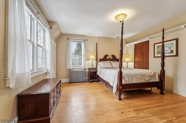 bedroom with radiator heating unit, light hardwood / wood-style floors, and multiple windows