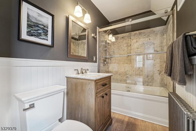 full bathroom featuring radiator heating unit, hardwood / wood-style floors, toilet, shower / bath combination with glass door, and vanity