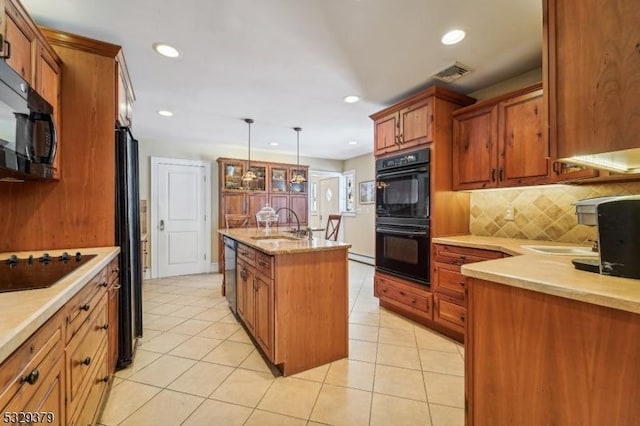 kitchen with backsplash, sink, black appliances, pendant lighting, and an island with sink