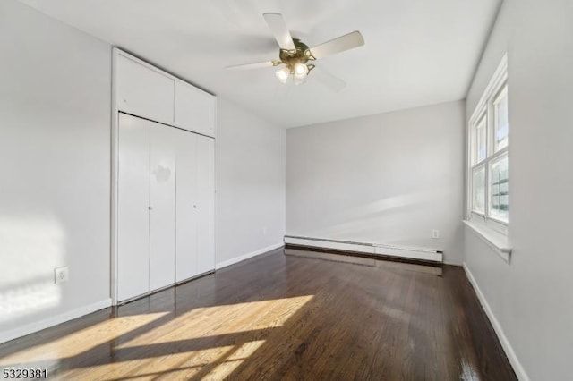 unfurnished bedroom with a closet, baseboard heating, dark wood-type flooring, and ceiling fan