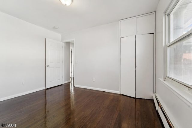 unfurnished bedroom with baseboard heating, a closet, and dark hardwood / wood-style floors