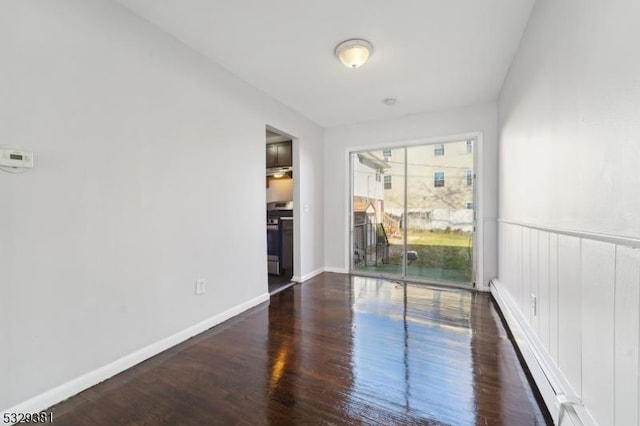 empty room with dark hardwood / wood-style flooring and a baseboard radiator