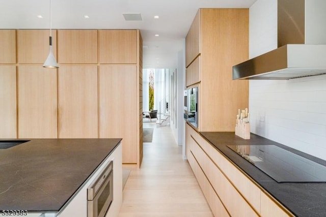 kitchen with light brown cabinets, light wood-type flooring, backsplash, and wall chimney range hood