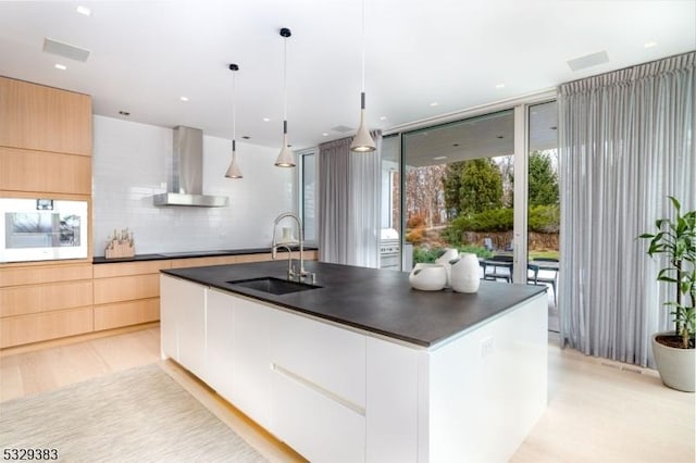 kitchen with sink, wall chimney range hood, backsplash, pendant lighting, and white cabinets