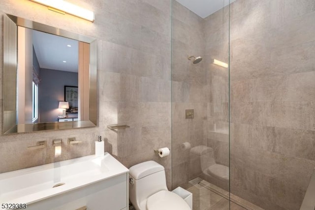 bathroom with tasteful backsplash, vanity, tiled shower, tile walls, and toilet