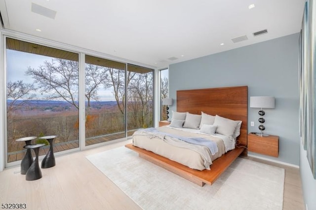 bedroom featuring light wood-type flooring, access to outside, and floor to ceiling windows