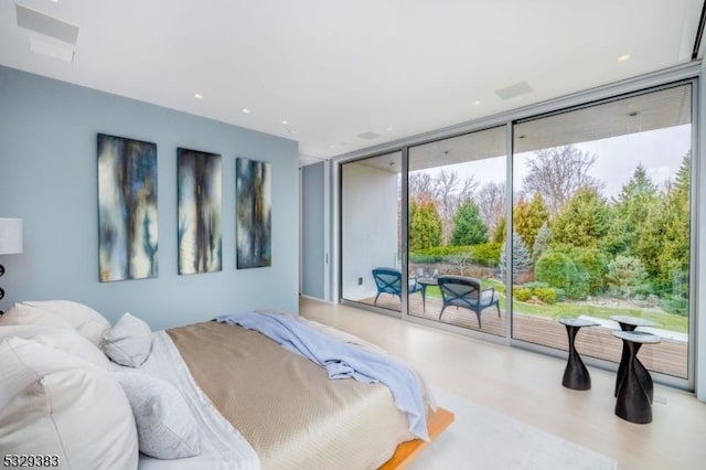 bedroom with access to outside, light wood-type flooring, and a wall of windows