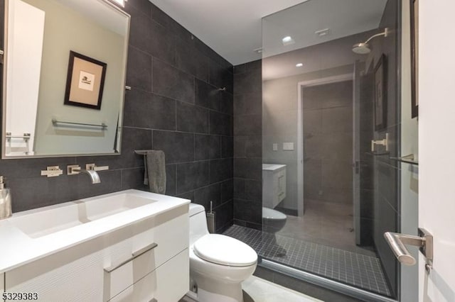 bathroom featuring vanity, backsplash, toilet, tiled shower, and tile walls