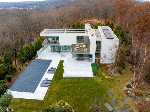 rear view of house with solar panels, a patio area, and a lawn