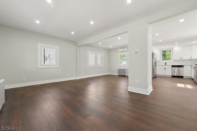 unfurnished living room with radiator heating unit, wood-type flooring, and a wall mounted air conditioner