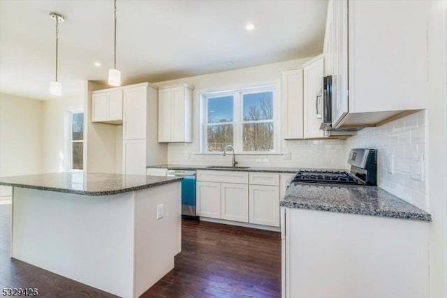 kitchen with appliances with stainless steel finishes, hanging light fixtures, a center island, white cabinets, and decorative backsplash