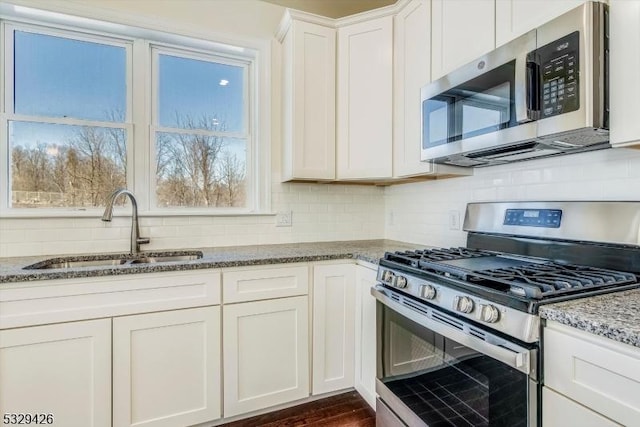 kitchen featuring white cabinetry, sink, decorative backsplash, dark stone counters, and stainless steel appliances