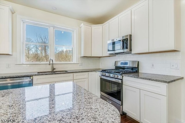 kitchen featuring appliances with stainless steel finishes, sink, white cabinets, backsplash, and light stone countertops