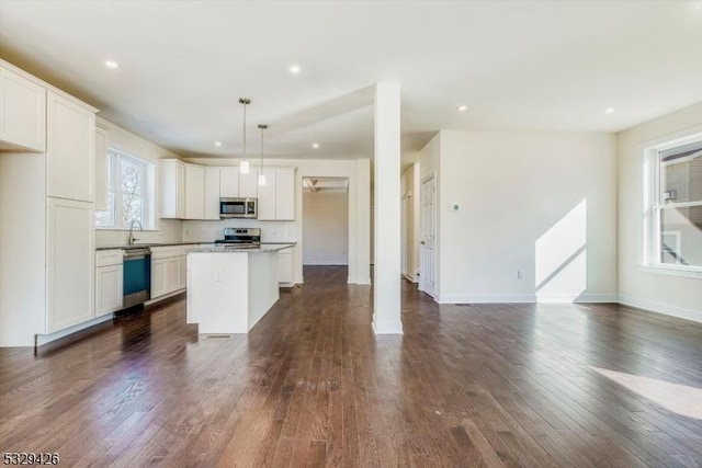 kitchen featuring appliances with stainless steel finishes, white cabinetry, a center island, light stone countertops, and decorative light fixtures