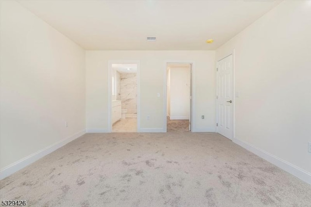 unfurnished bedroom with light colored carpet, a closet, and ensuite bathroom