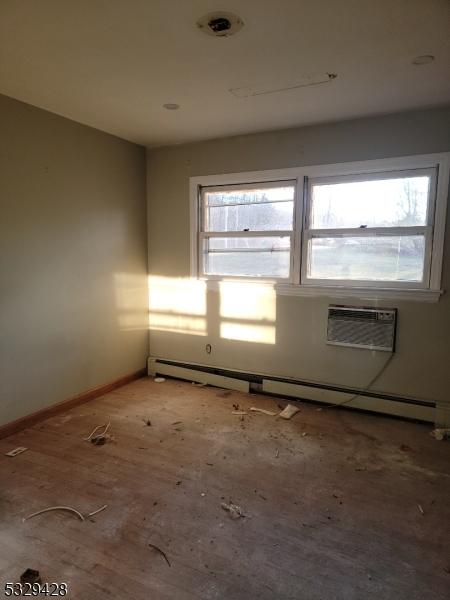 empty room featuring baseboard heating, a wall mounted air conditioner, and hardwood / wood-style flooring