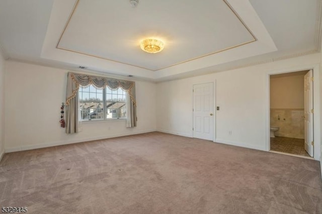 unfurnished bedroom featuring a raised ceiling, ensuite bath, and carpet floors