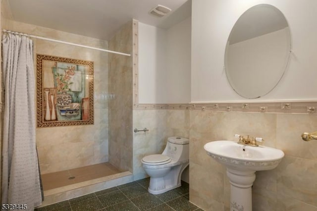 bathroom featuring tile patterned floors, sink, toilet, tile walls, and walk in shower