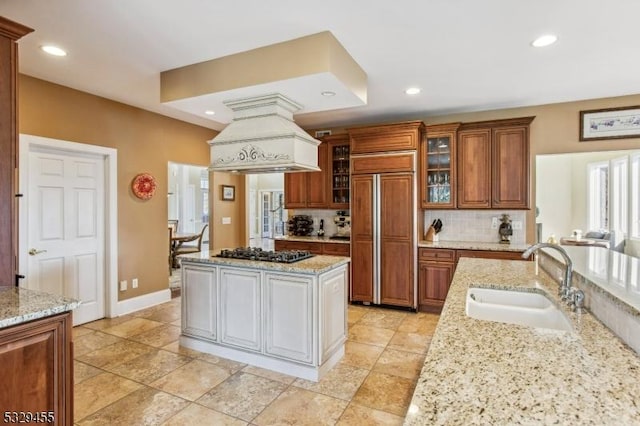 kitchen featuring light stone countertops, premium range hood, sink, paneled built in refrigerator, and stainless steel gas stovetop