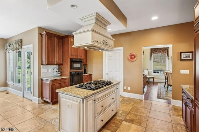 kitchen with tasteful backsplash, light stone counters, custom range hood, a kitchen island, and stainless steel gas stovetop