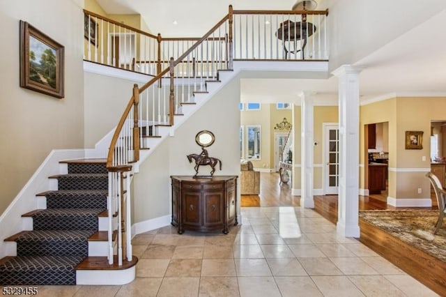 tiled entryway featuring decorative columns, crown molding, and a high ceiling