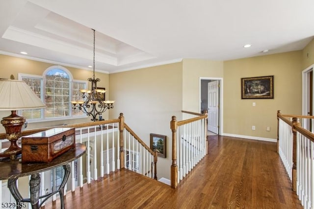 hall with a raised ceiling, crown molding, dark hardwood / wood-style floors, and an inviting chandelier