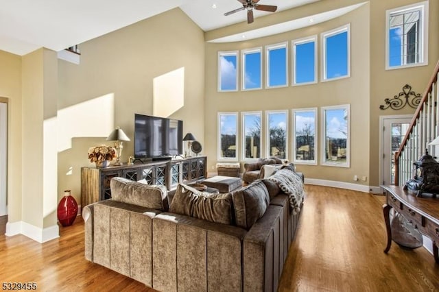 living room with hardwood / wood-style flooring, ceiling fan, and a towering ceiling