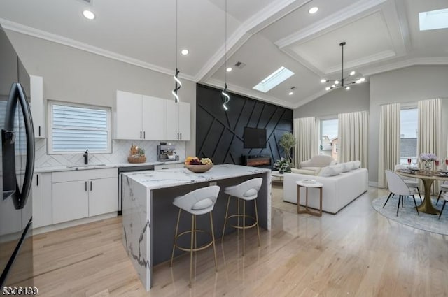 kitchen featuring fridge with ice dispenser, sink, a kitchen island, lofted ceiling with skylight, and white cabinets