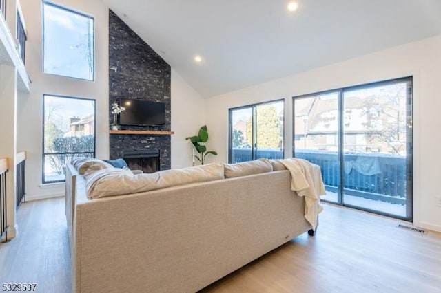 living room with light wood-type flooring, high vaulted ceiling, a stone fireplace, and a wealth of natural light