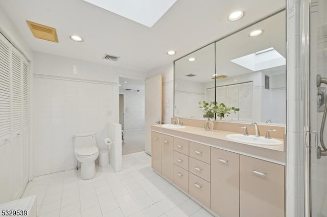 bathroom featuring a shower with shower door, a skylight, vanity, toilet, and tile patterned floors