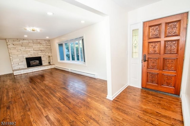 foyer entrance with wood-type flooring, a baseboard radiator, and a stone fireplace