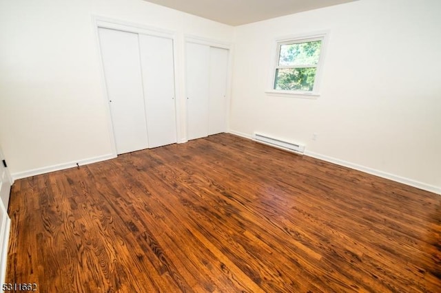 unfurnished bedroom featuring dark hardwood / wood-style flooring, multiple closets, and a baseboard heating unit