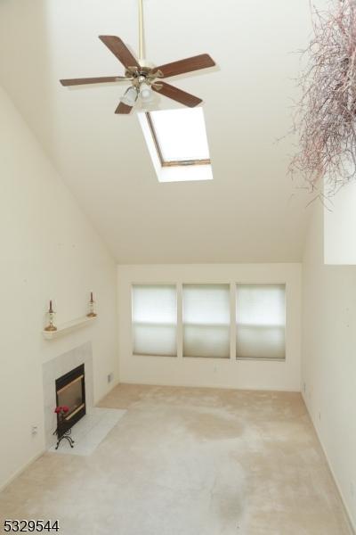 unfurnished living room with vaulted ceiling with skylight, a fireplace, light colored carpet, and ceiling fan