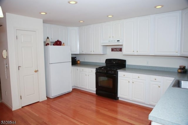 kitchen with under cabinet range hood, black range with gas cooktop, white cabinets, and freestanding refrigerator