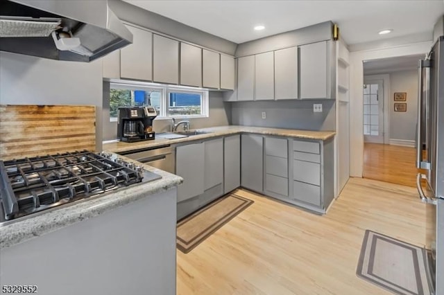 kitchen with sink, gray cabinetry, stainless steel appliances, wall chimney range hood, and light wood-type flooring