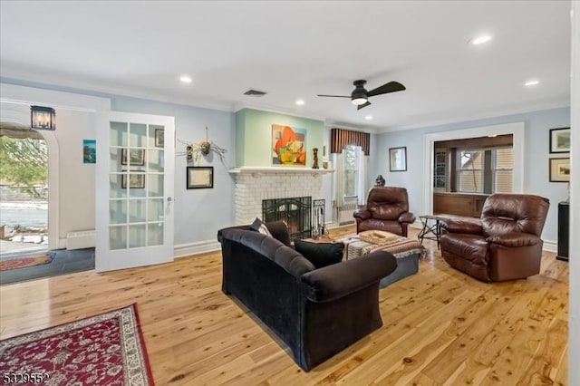 living room featuring crown molding, ceiling fan, a brick fireplace, and light hardwood / wood-style flooring