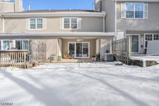 snow covered back of property featuring central AC unit and stucco siding