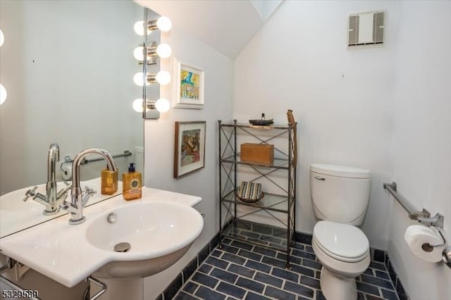 bathroom featuring toilet, lofted ceiling, and sink