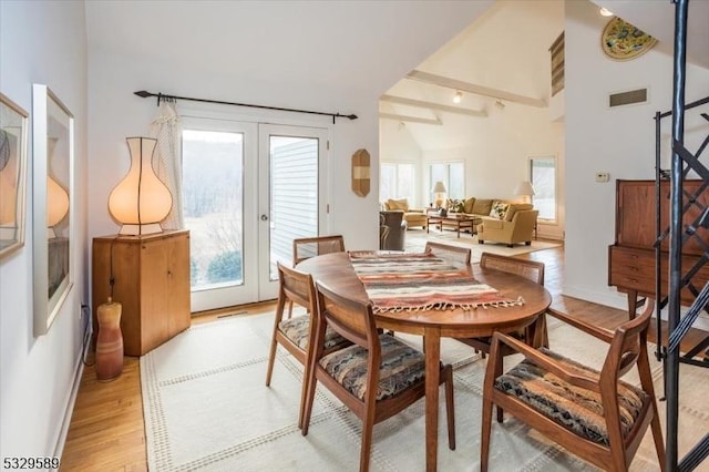 dining space with beam ceiling, light wood-type flooring, high vaulted ceiling, and french doors