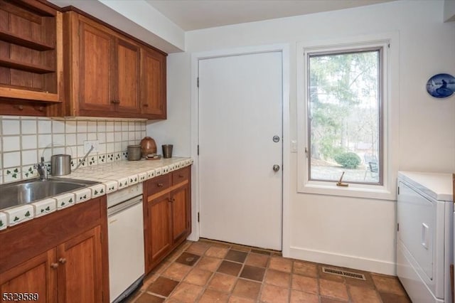 kitchen with washer / dryer, backsplash, white dishwasher, and sink