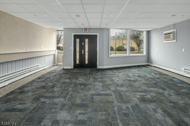 interior space featuring a paneled ceiling, a wall mounted air conditioner, and a baseboard heating unit