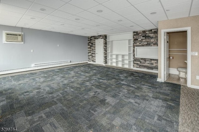 interior space with dark colored carpet, baseboard heating, a wall unit AC, and a drop ceiling