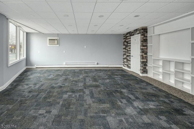 carpeted spare room with a baseboard radiator, an AC wall unit, and a drop ceiling