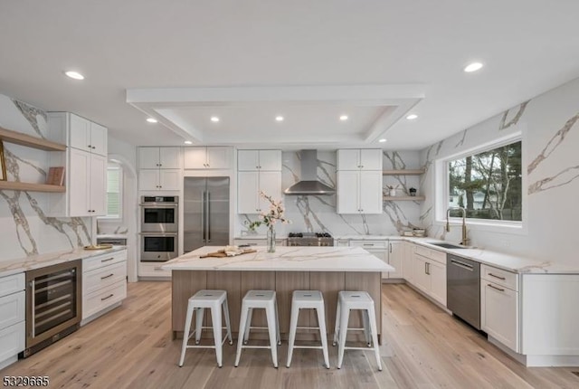 kitchen with appliances with stainless steel finishes, a kitchen island with sink, wall chimney exhaust hood, and open shelves