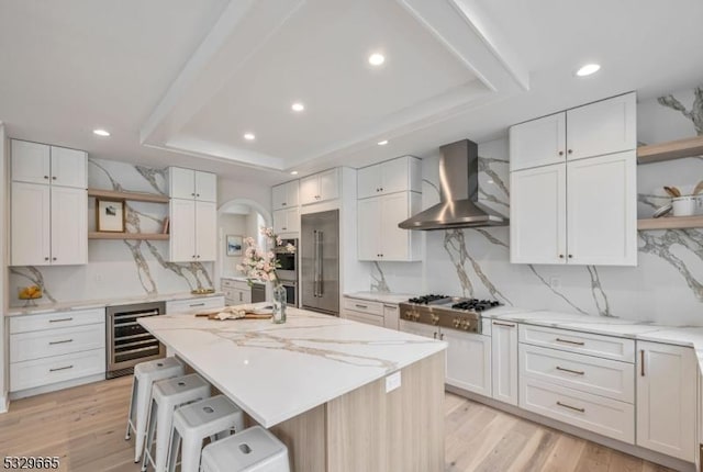 kitchen featuring beverage cooler, stainless steel appliances, a kitchen island, wall chimney range hood, and open shelves