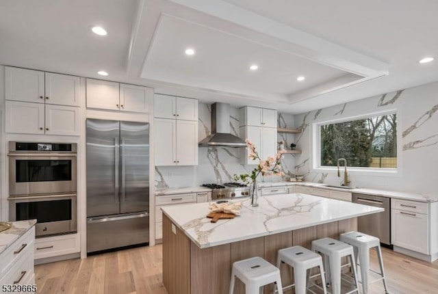 kitchen with white cabinets, wall chimney exhaust hood, stainless steel appliances, and a center island