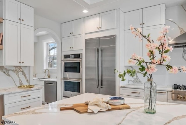 kitchen featuring appliances with stainless steel finishes, white cabinets, a sink, and light stone countertops