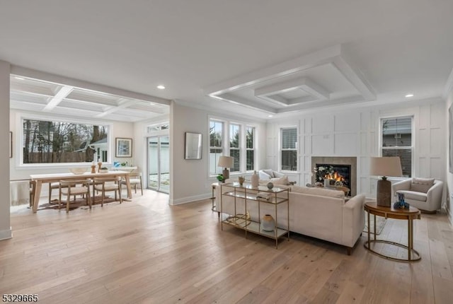 living area featuring coffered ceiling, baseboards, light wood-type flooring, beamed ceiling, and a glass covered fireplace