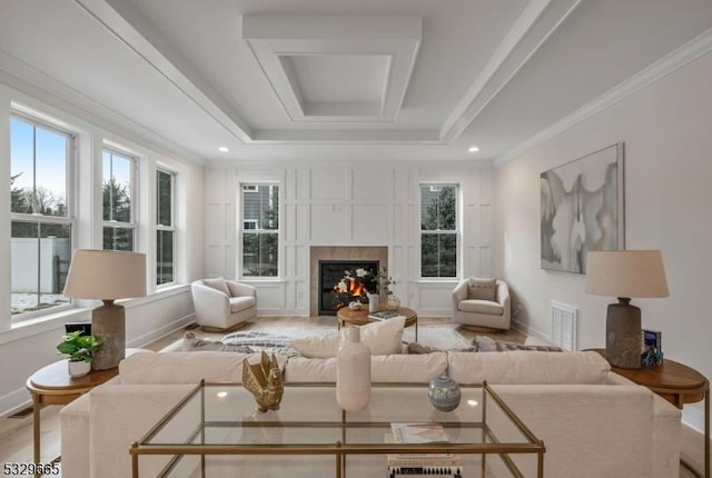 interior space featuring baseboards, a glass covered fireplace, a raised ceiling, and a healthy amount of sunlight